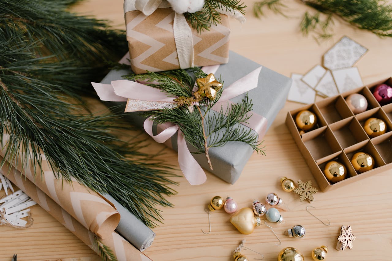 Beautifully wrapped Christmas gifts with ornaments and pine branches on a wooden table.