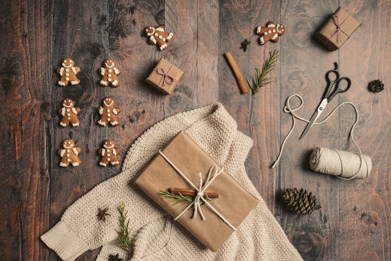 Flat lay featuring Christmas gifts, gingerbread cookies, and festive decor on wooden surface.