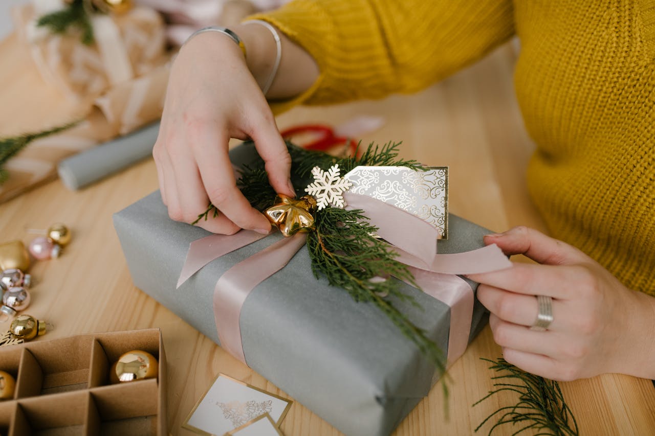 Close-up of hands wrapping a Christmas gift with ribbon and festive decorations.